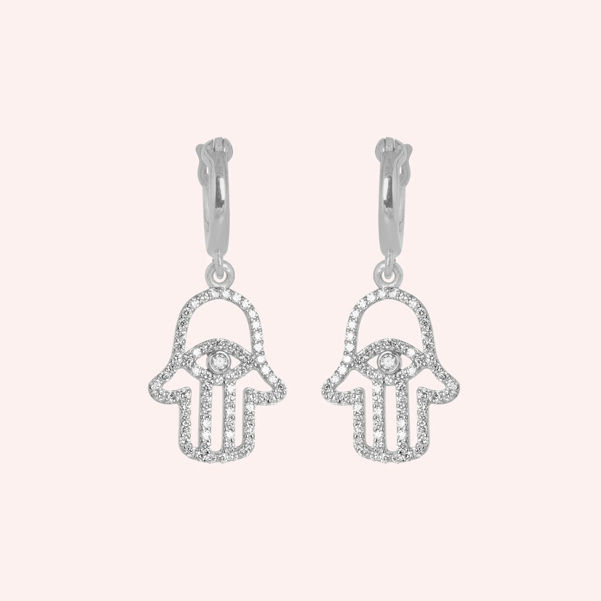 Hoop_earrings_in_sterling_silver_with_a_hamsa_hand_design_at_front_angle_view_on_solid_pink_background