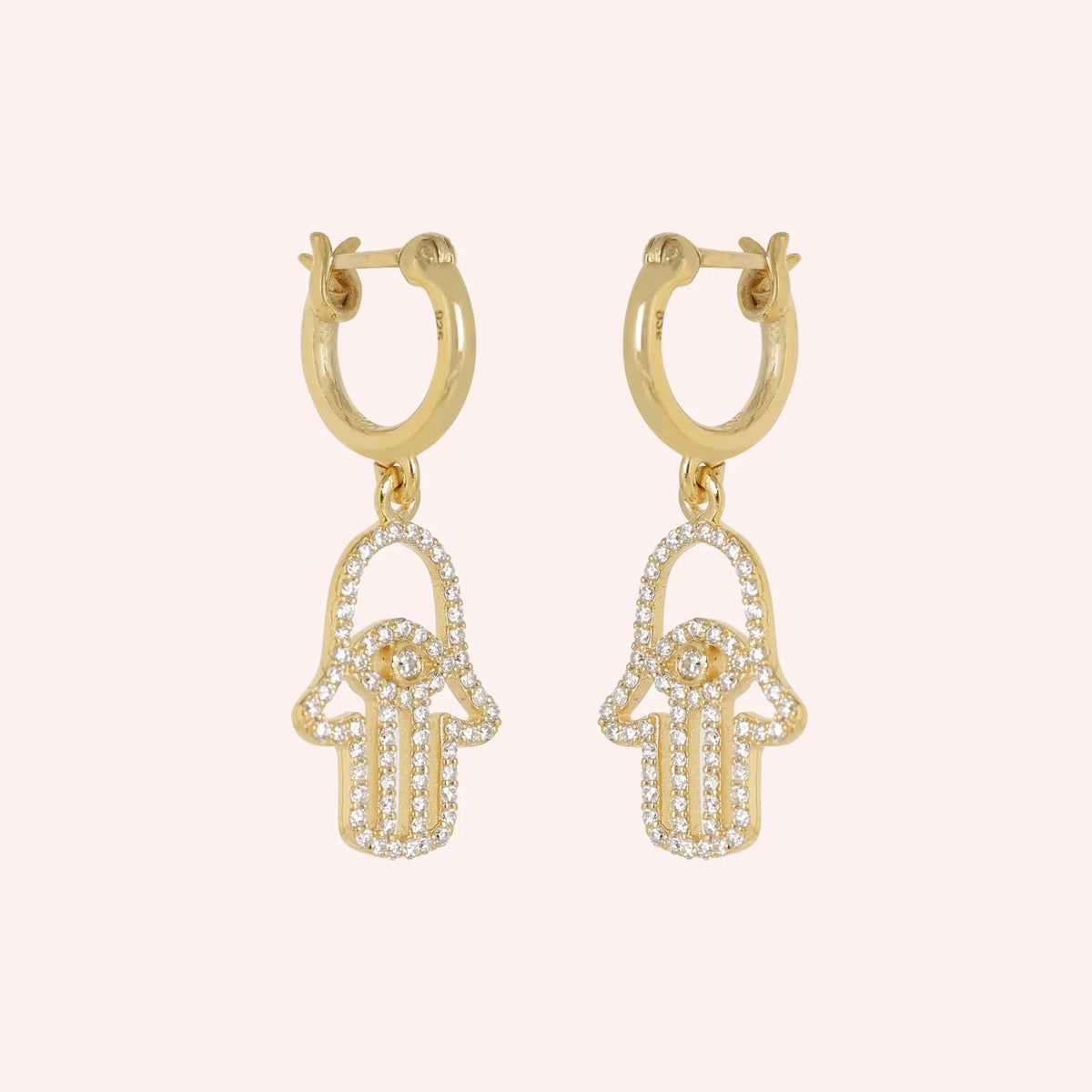 Hoop_earrings_in_gold_plated_silver_with_a_hamsa_hand_design_at_slight_angle_view_on_solid_pink_background
