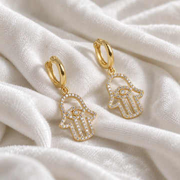 Hoop_earrings_in_gold_plated_silver_with_hamsa_hand_design_and_CZ_stones_at_side_angle_view_on_soft_fabric_background