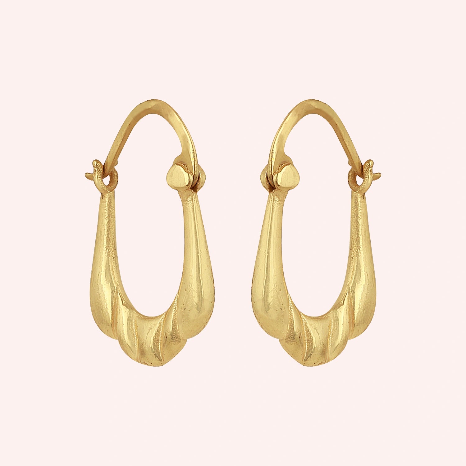 Huggie_earrings_in_gold_plated_silver_with_handcrafted_teardrop_hoops_at_slight_angle_on_solid_pink_background