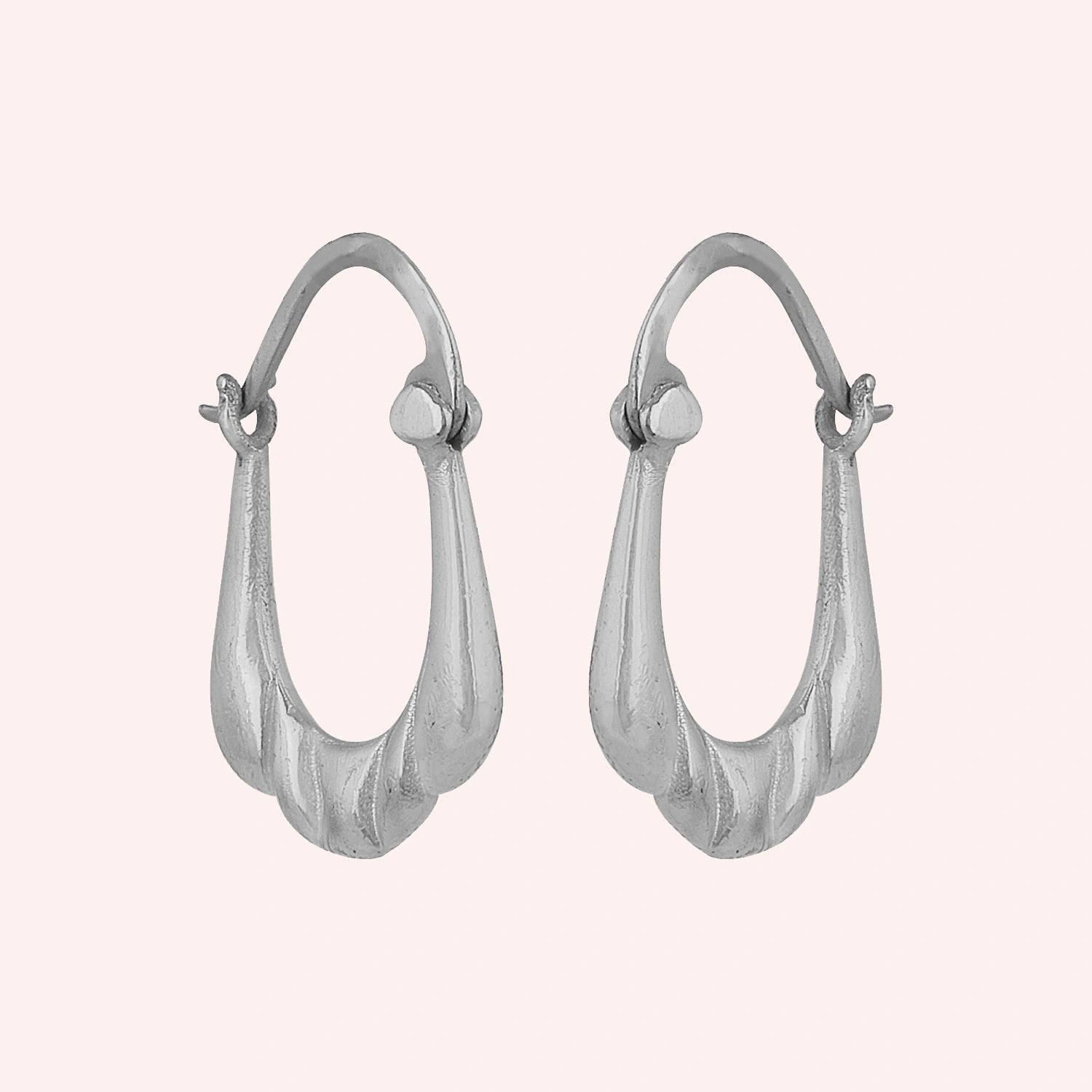 Huggie_earrings_in_sterling_silver_with_handcrafted_teardrop_hoops_at_slight_angle_on_solid_pink_background