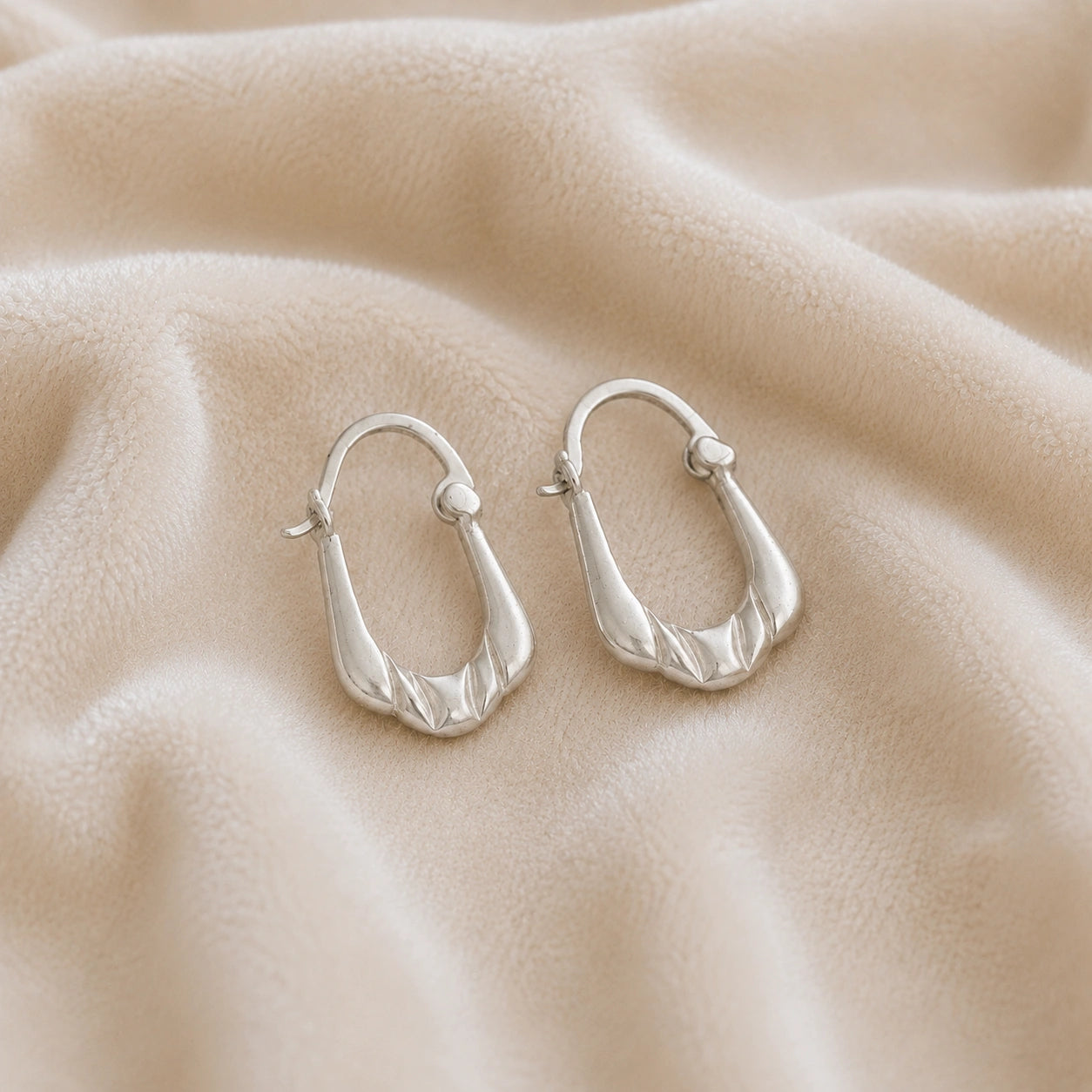 Huggie_earrings_in_sterling_silver_with_handcrafted_teardrop_hoops_at_slight_angle_on_soft_fabric_background