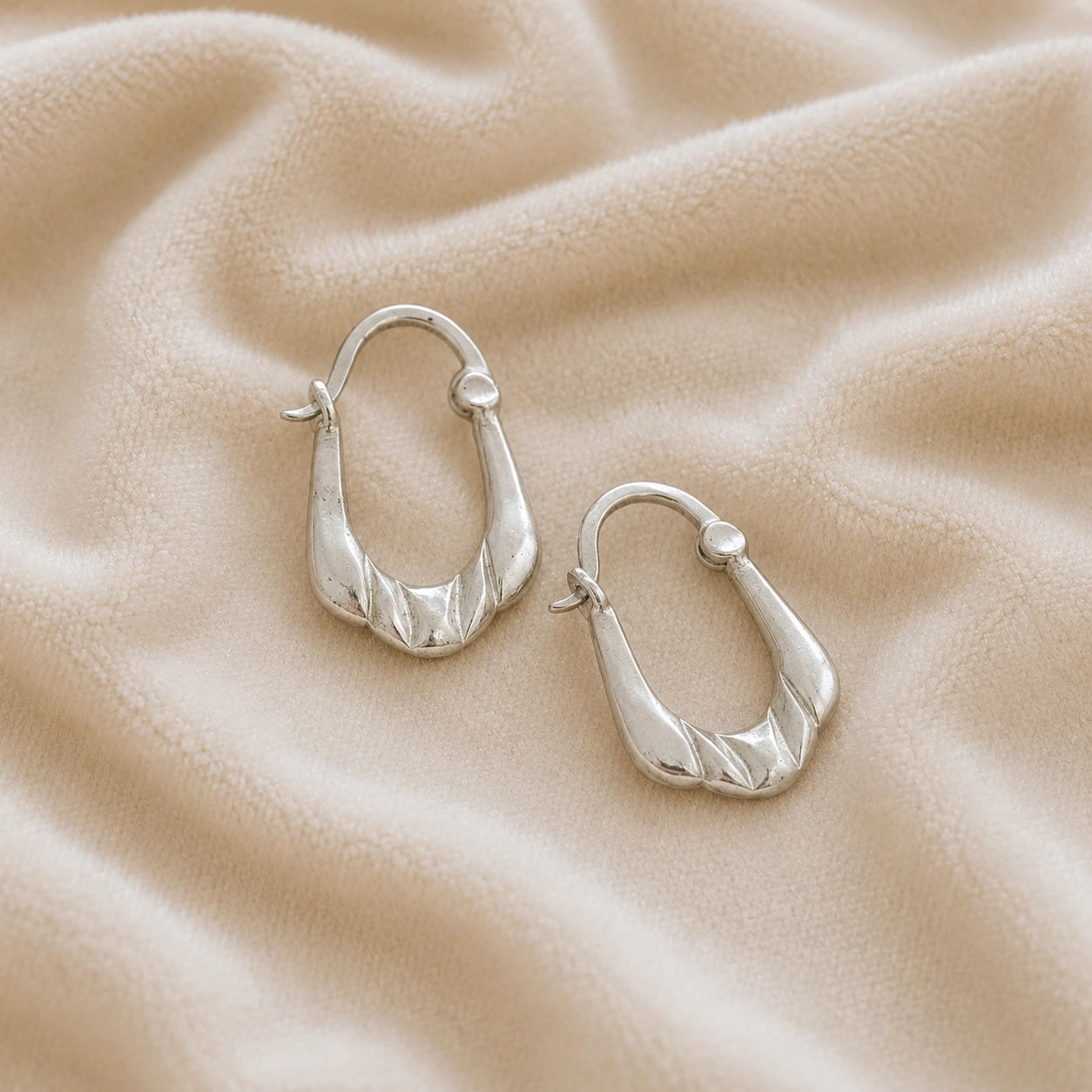 Huggie_earrings_in_sterling_silver_with_handcrafted_teardrop_hoops_at_slight_angle_on_soft_fabric_background