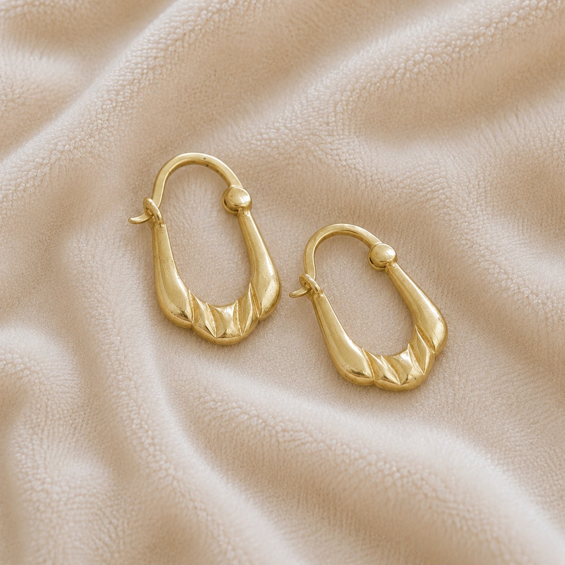 Huggie_earrings_in_gold_plated_silver_with_handcrafted_teardrop_hoops_at_slight_angle_on_soft_fabric_background