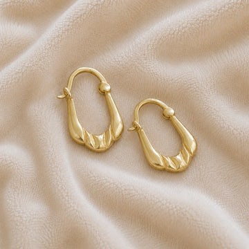 Huggie_earrings_in_gold_plated_silver_with_handcrafted_teardrop_hoops_at_slight_angle_on_soft_fabric_background