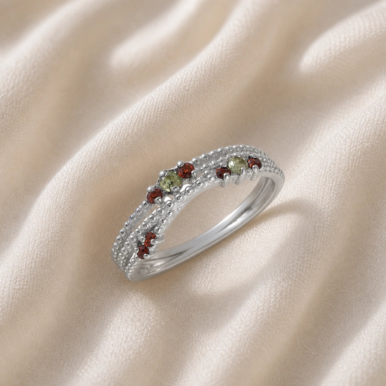 Infinity_ring_sterling_silver_band_with_red_and_green_stones_slightly_angled_view_on_soft_fabric_background
