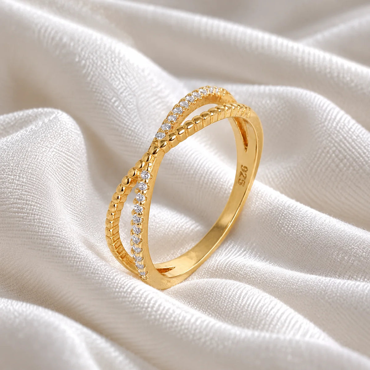 Infinity_ring_in_gold_plated_silver_with_criss_cross_design_and_lab_grown_diamonds_at_side_angle_view_on_soft_fabric_background