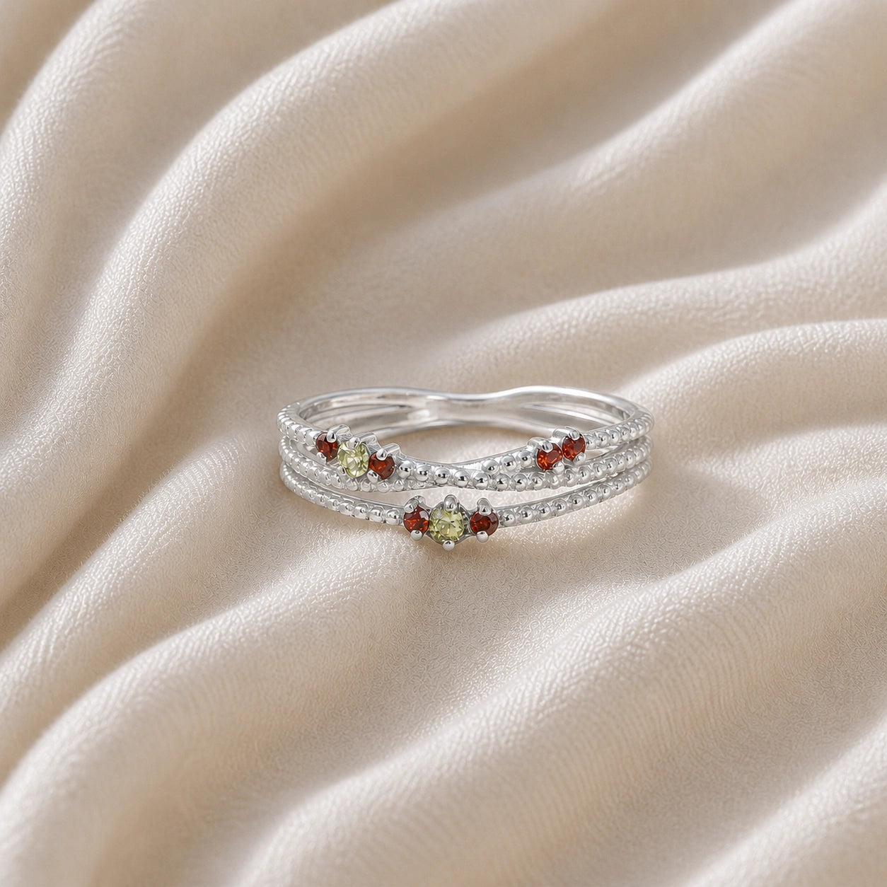 Infinity_ring_sterling_silver_band_with_red_and_green_stones_front_angle_view_on_soft_fabric_background