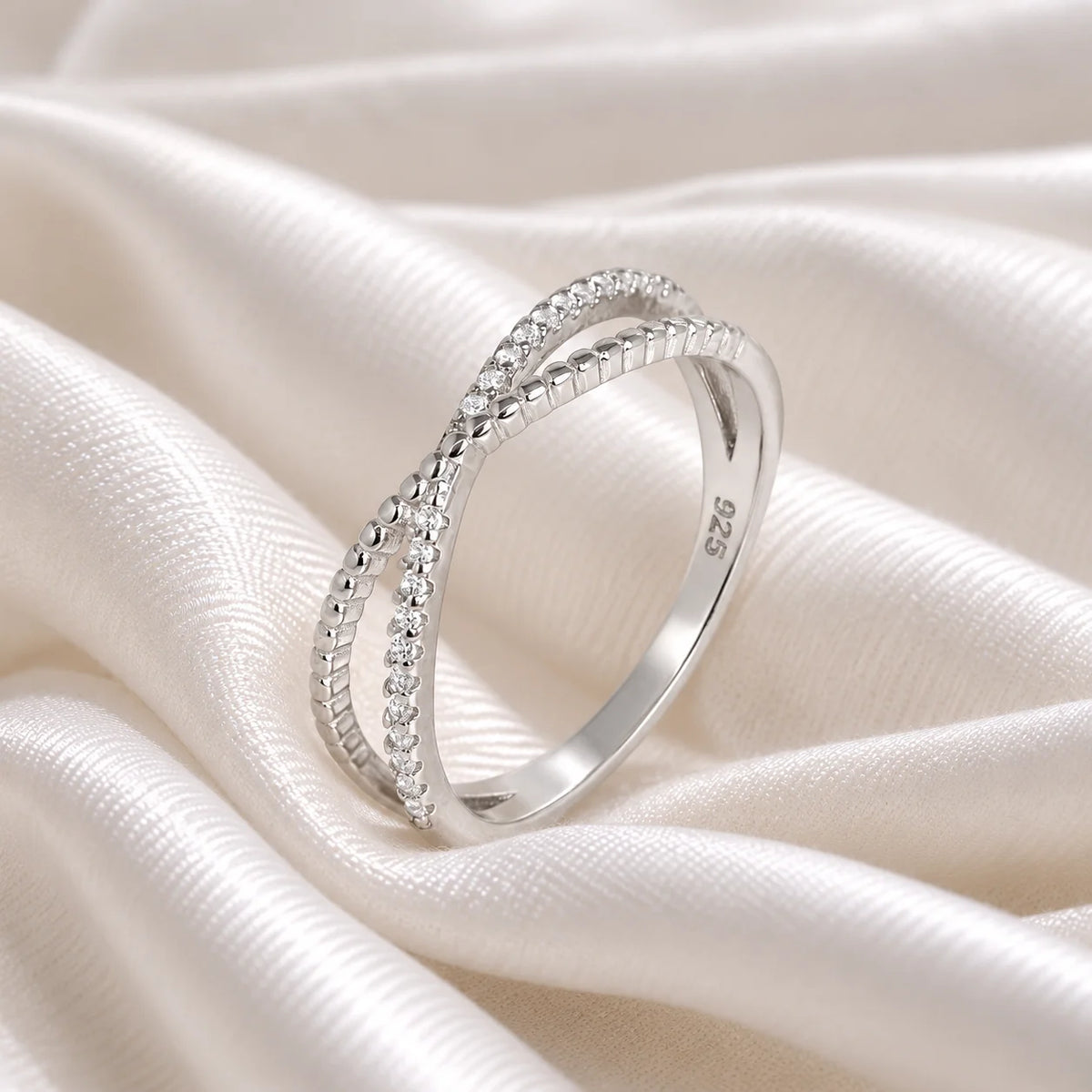 Infinity_ring_in_s_silver_with_criss_cross_design_and_lab_grown_diamonds_at_side_angle_view_on_soft_fabric_background