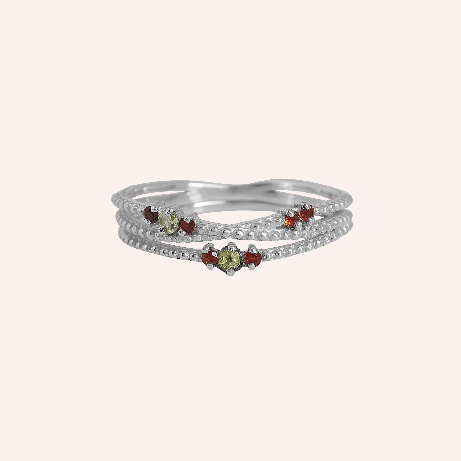 Infinity_ring_sterling_silver_band_with_red_and_green_stones_front_angle_view_on_solid_pink_background