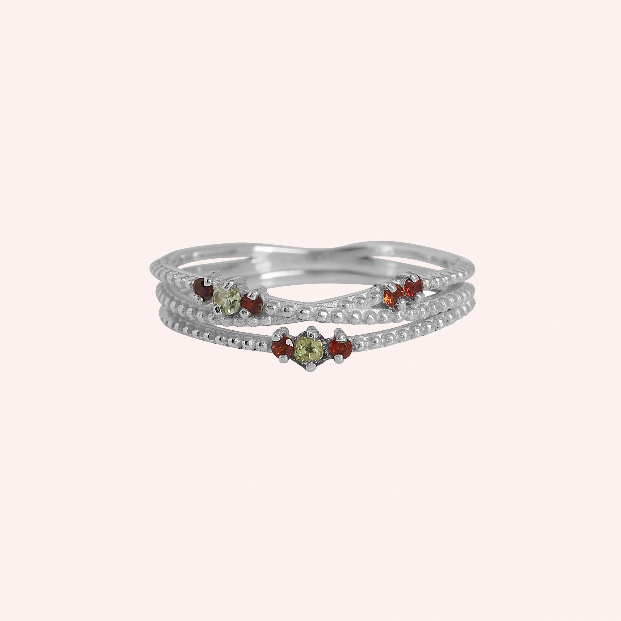 Infinity_ring_sterling_silver_band_with_red_and_green_stones_front_angle_view_on_solid_pink_background