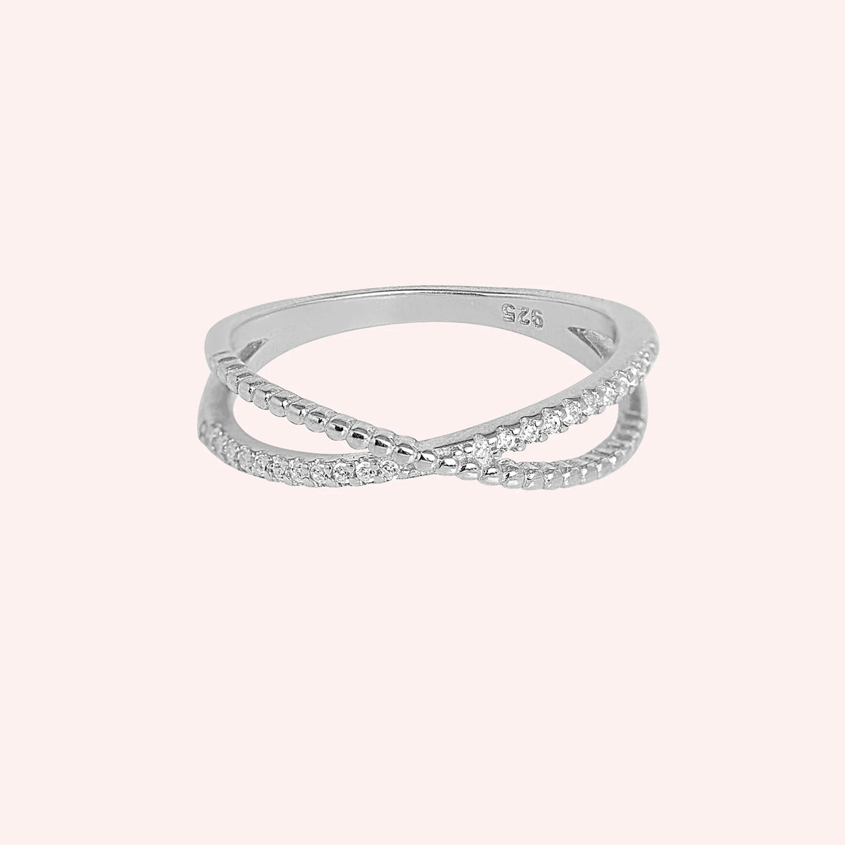Infinity_ring_in_sterling_silver_with_criss_cross_design_and_lab_grown_diamonds_at_front_angle_view_on_solid_pink_background