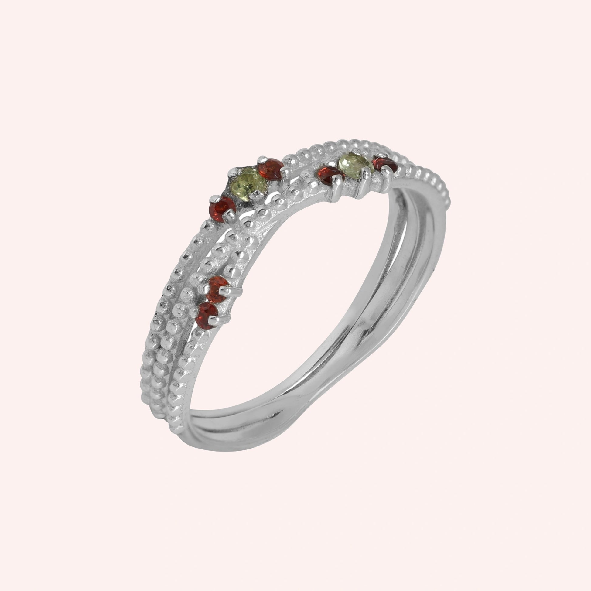 Infinity_ring_sterling_silver_band_with_red_and_green_stones_slightly_angled_view_on_solid_pink_background