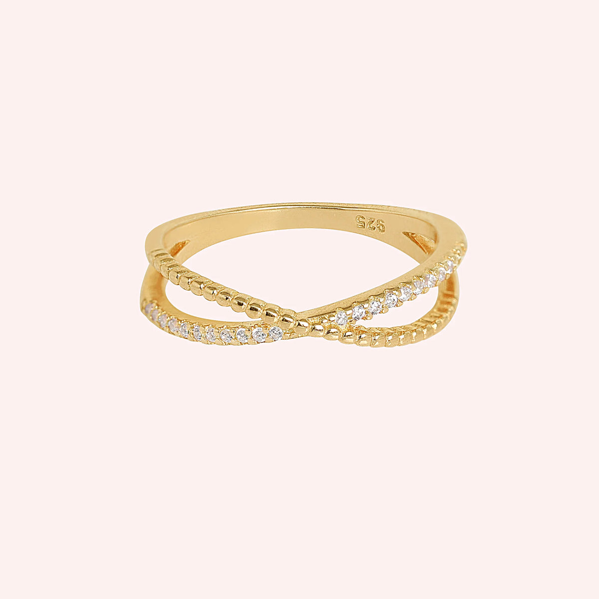 Infinity_ring_in_gold_plated_silver_with_criss_cross_design_and_lab_grown_diamonds_at_front_angle_view_on_solid_pink_background