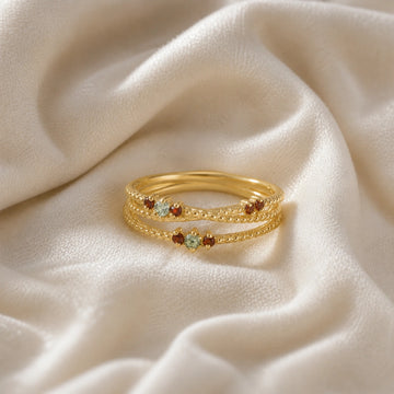 Infinity_ring_gold_plated_silver_band_with_red_and_green_stones_front_angle_view_on_soft_fabric_background