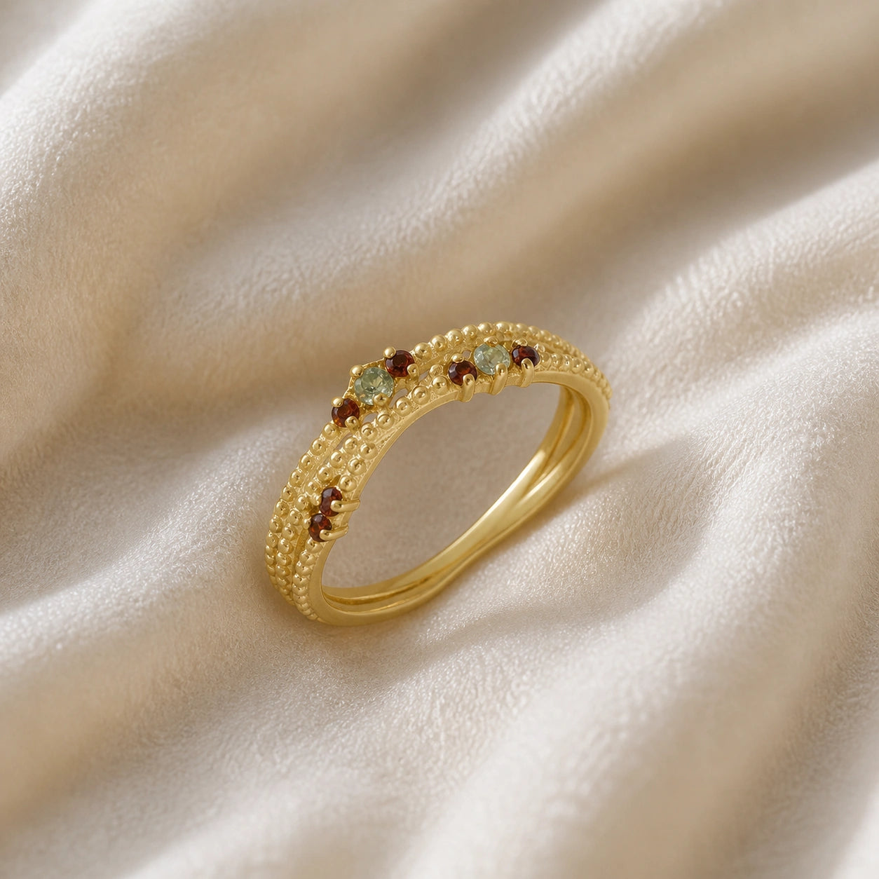 Infinity_ring_gold_plated_silver_band_with_red_and_green_stones_slightly_angled_view_on_soft_fabric_background