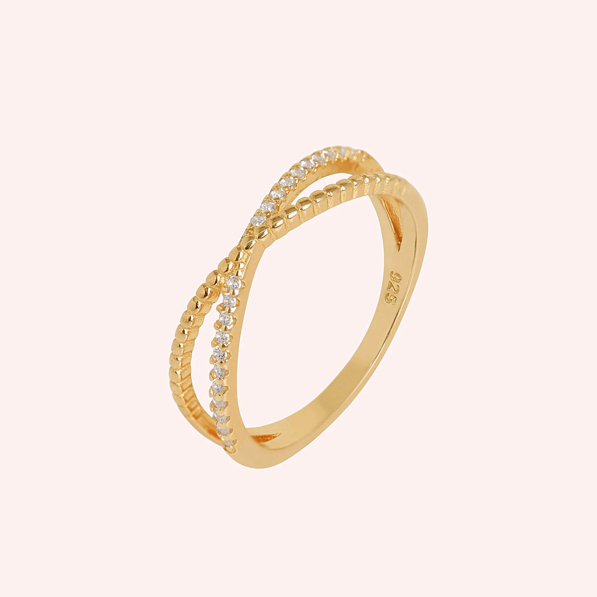 Infinity_ring_in_gold_plated_silver_with_criss_cross_design_and_lab_grown_diamonds_at_side_angle_view_on_solid_pink_background