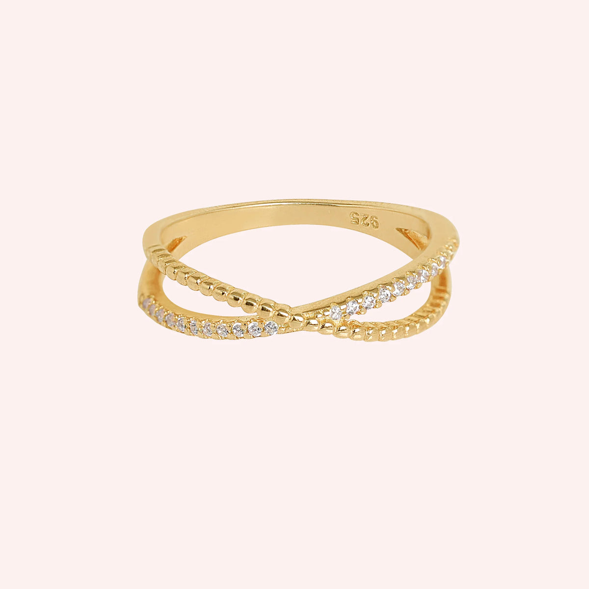 Infinity_ring_in_gold_plated_silver_with_criss_cross_design_and_CZ_stones_at_front_angle_view_on_solid_pink_background
