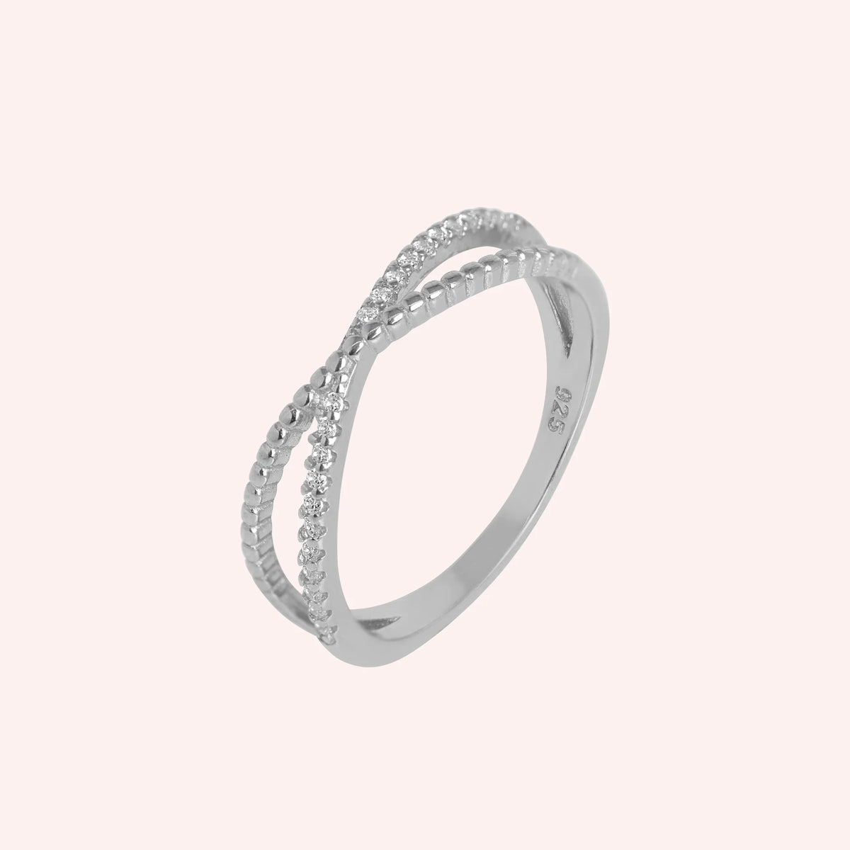 Infinity_ring_in_sterling_silver_with_criss_cross_design_and_CZ_stones_at_side_angle_view_on_solid_pink_background