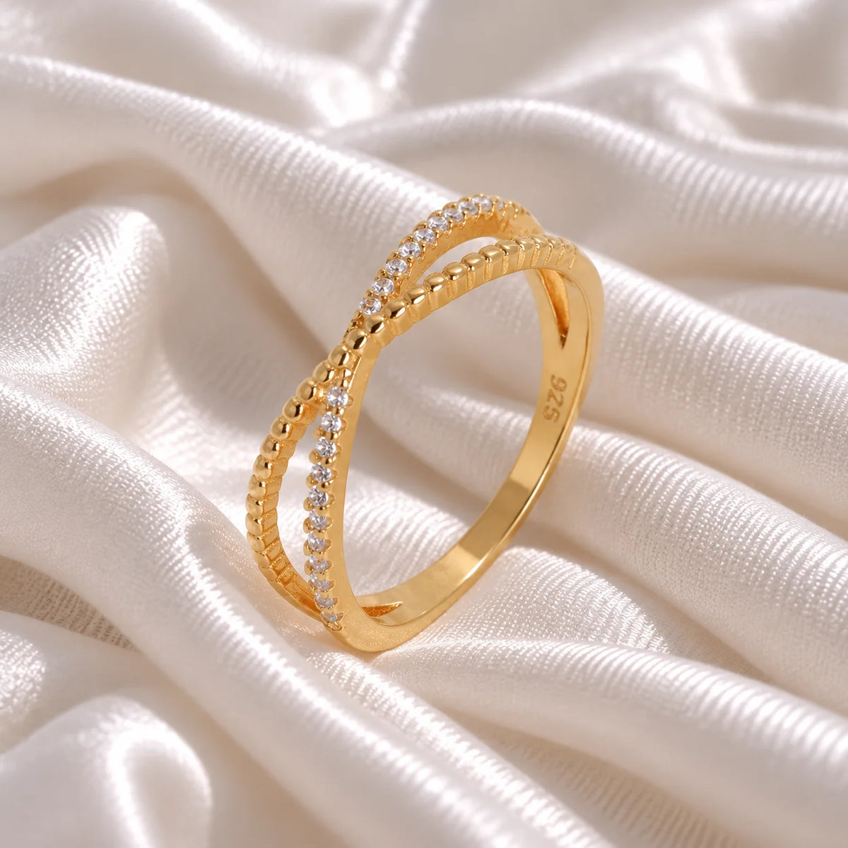 Infinity_ring_in_gold_plated_silver_with_criss_cross_design_and_CZ_stones_at_side_angle_view_on_soft_fabric_background