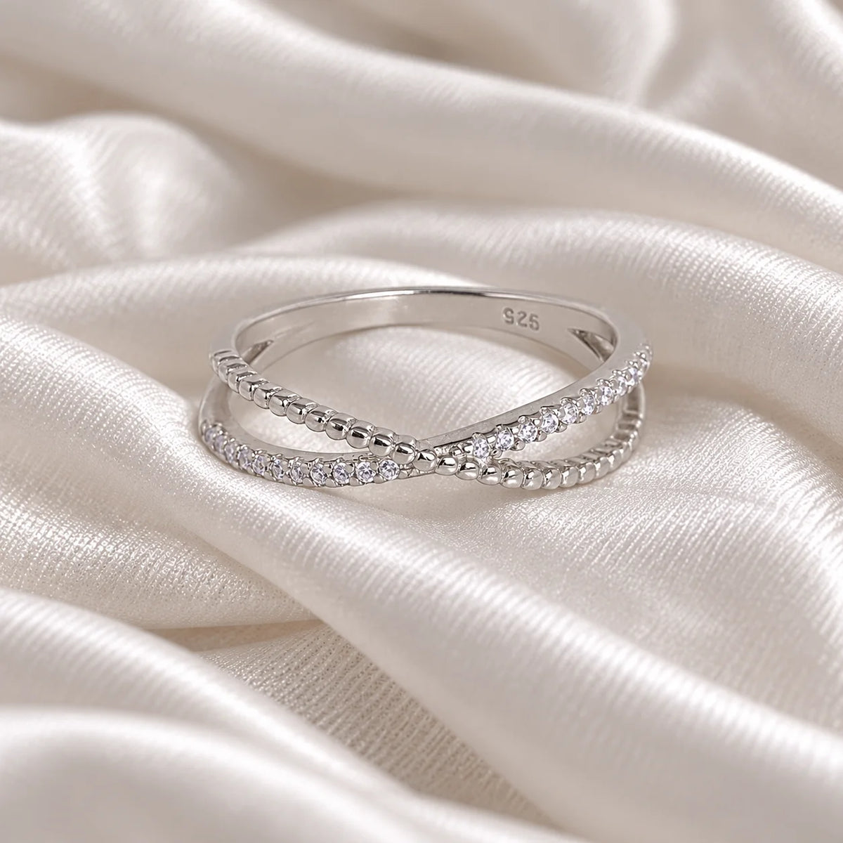 Infinity_ring_in_sterling_silver_with_criss_cross_design_and_CZ_stones_at_front_angle_view_on_soft_fabric_background