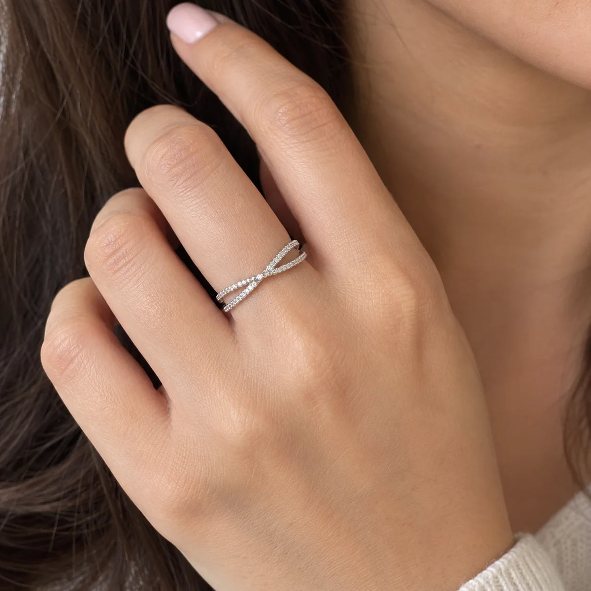 Infinity_ring_in_sterling_silver_with_criss_cross_design_and_CZ_stones_at_front_angle_view_worn_by_a_model