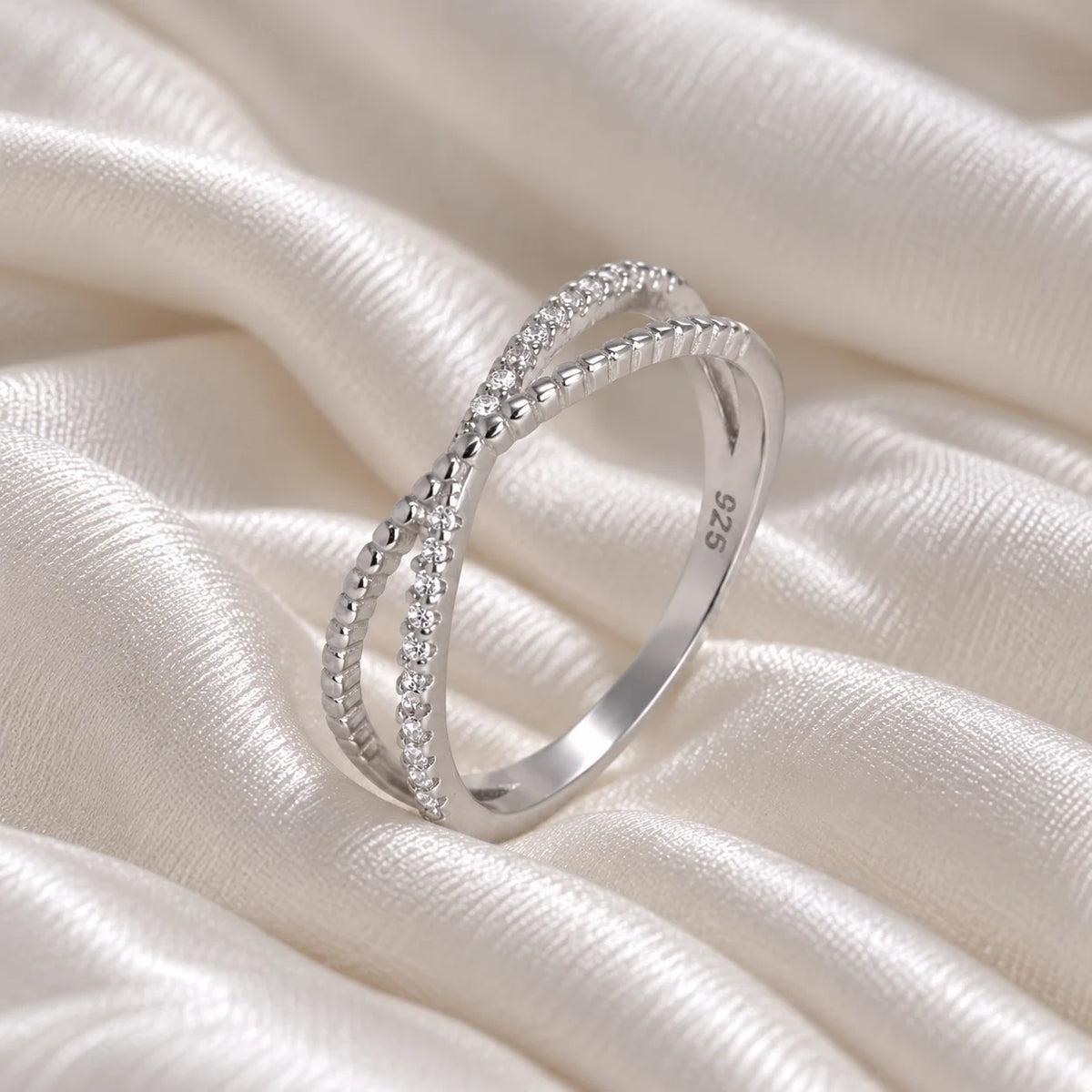 Infinity_ring_in_sterling_silver_with_criss_cross_design_and_CZ_stones_at_side_angle_view_on_soft_fabric_background