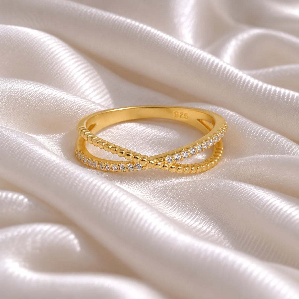 Infinity_ring_in_gold_plated_silver_with_criss_cross_design_and_CZ_stones_at_front_angle_view_on_soft_fabric_background