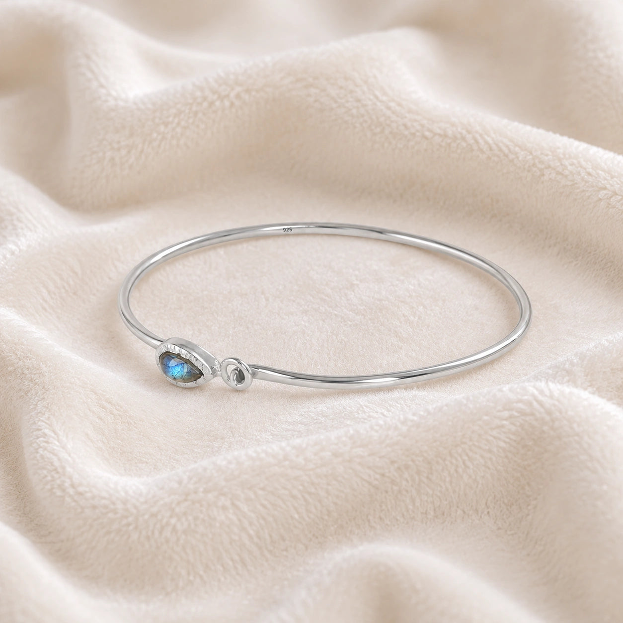 Labradorite_bracelet_in_sterling_silver_with_an_teardrop_labradorite_stone_at_slight_angle_view_on_soft_fabric_background