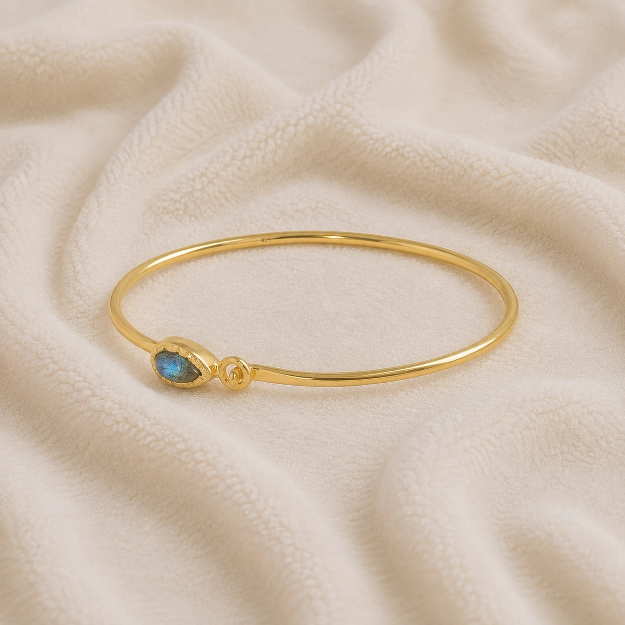 Labradorite_bracelet_in_gold_plated_silver_with_an_teardrop_labradorite_stone_at_slight_angle_view_on_soft_fabric_background