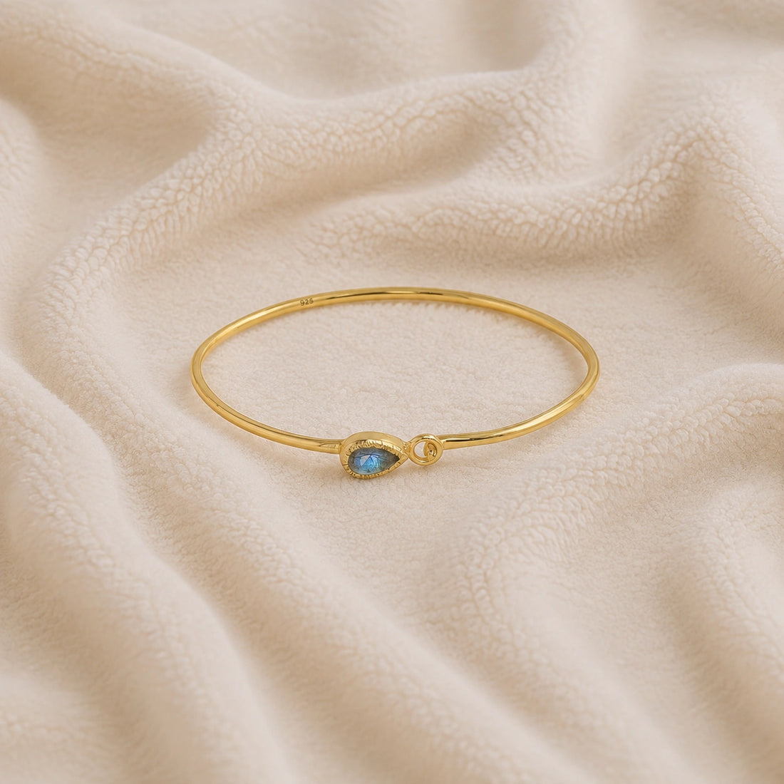 Labradorite_bracelet_in_gold_plated_silver_with_an_teardrop_labradorite_stone_at_front_angle_view_on_soft_fabric_background