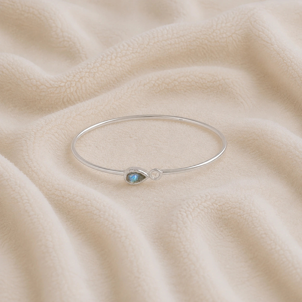 Labradorite_bracelet_in_sterling_silver_with_an_teardrop_labradorite_stone_at_front_angle_view_on_soft_fabric_background