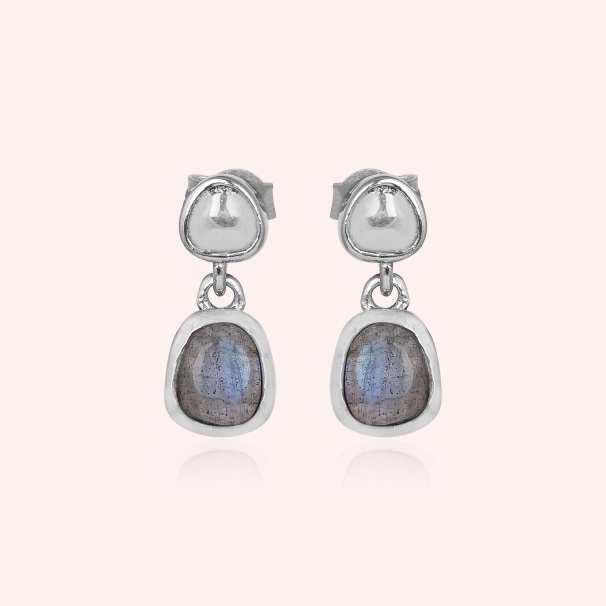 Tiny earrings featuring silver drop design with labradorite charm stones viewed straight on a light pink background