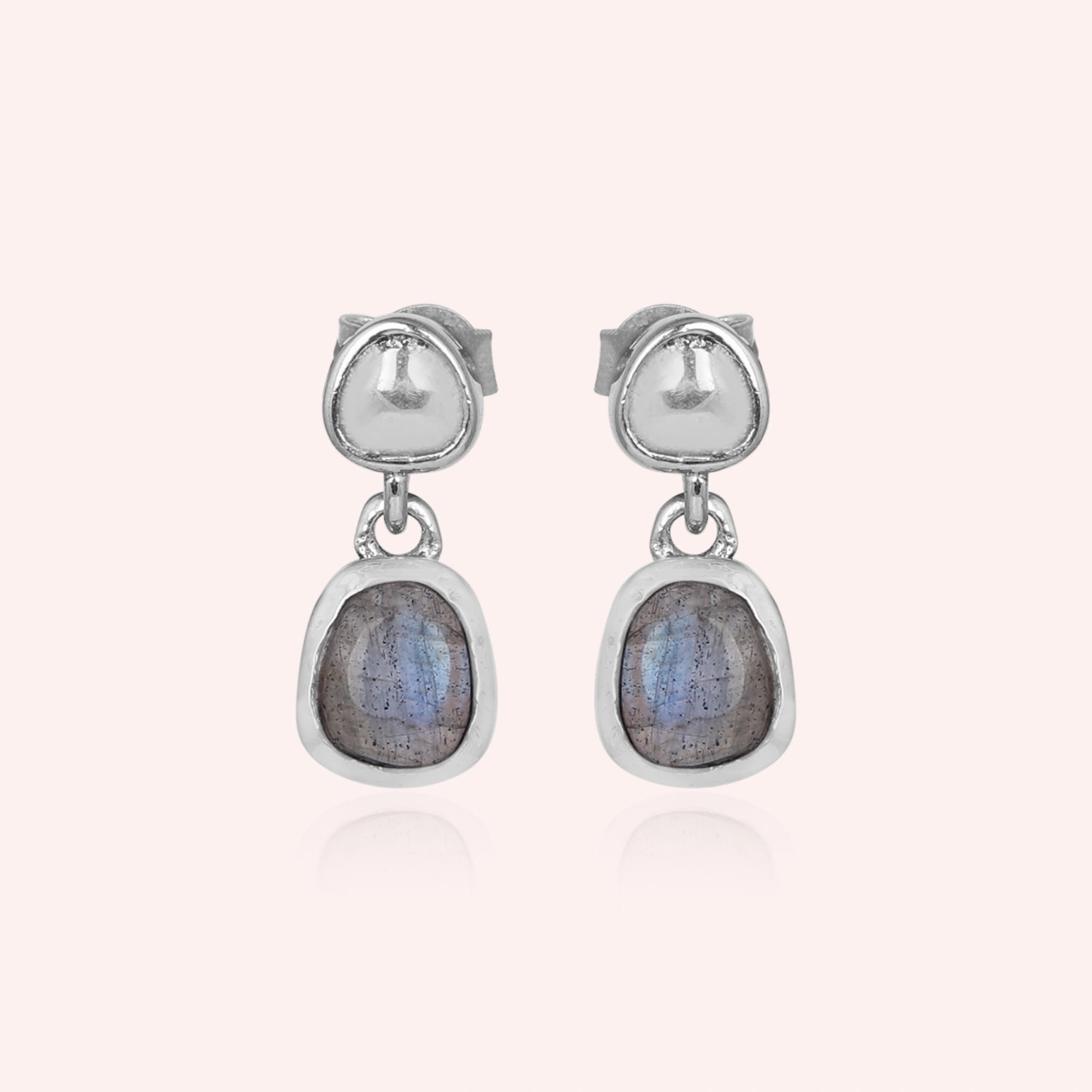 Tiny earrings featuring silver drop design with labradorite charm stones viewed straight on a light pink background