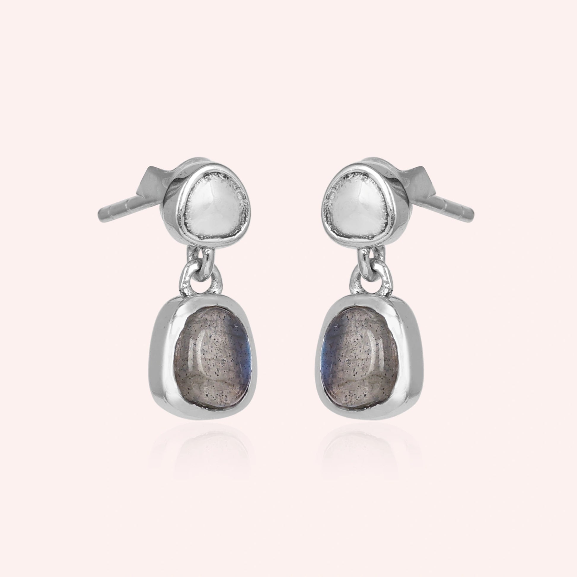 Tiny earrings featuring silver drop design with labradorite charm stones viewed on a slight angle with light pink background