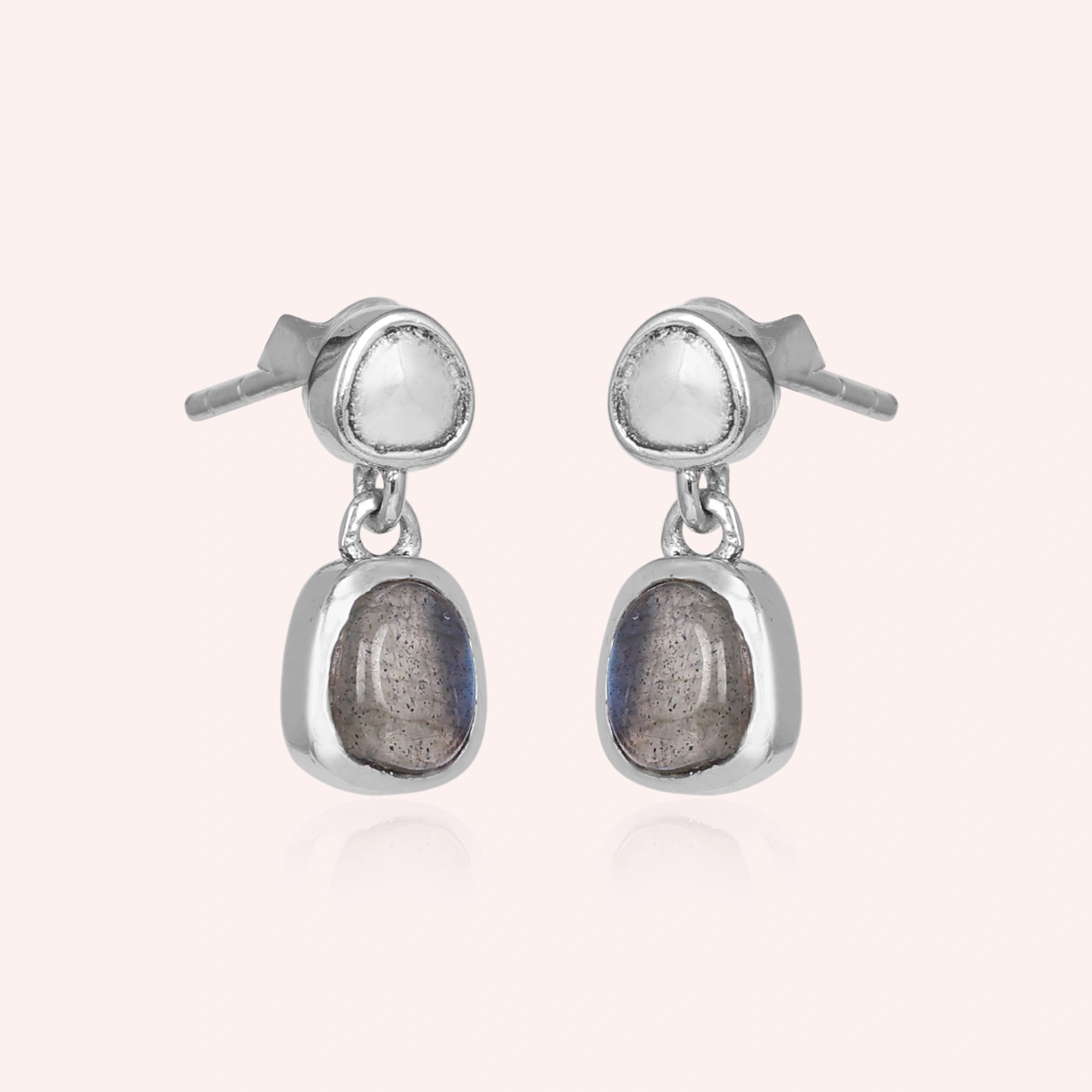 Tiny earrings featuring silver drop design with labradorite charm stones viewed on a slight angle with light pink background