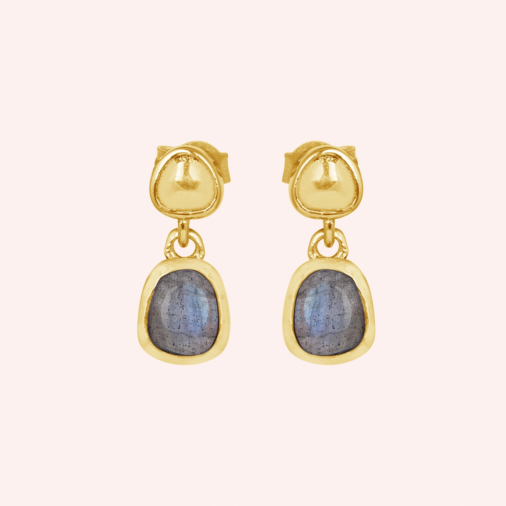 Tiny earrings featuring gold plated studs with labradorite charm stones viewed straight on a light pink surface