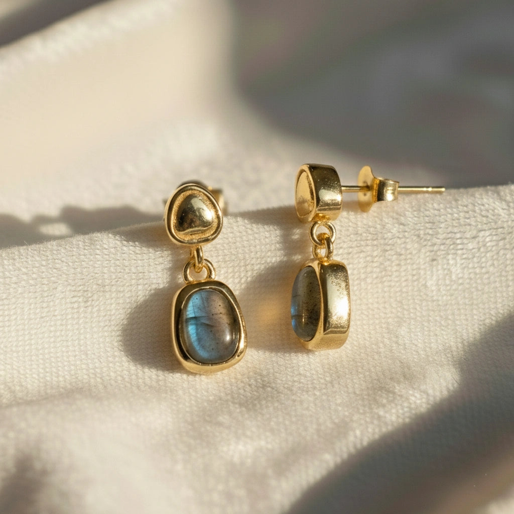 Tiny earrings featuring gold-plated studs with labradorite charm stones angled downward on soft white draped fabric
