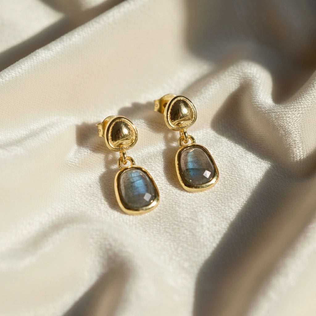 Tiny earrings featuring gold-plated studs with labradorite charm stones angled downward on soft white draped fabric