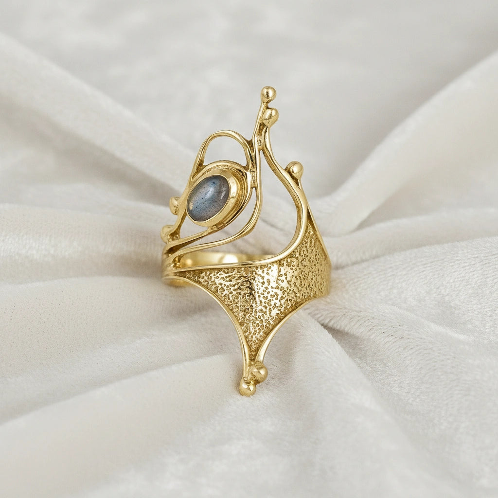 Gold plated sterling silver labradorite ring with a sculptural design an oval gemstone viewed slightly angled on pink background