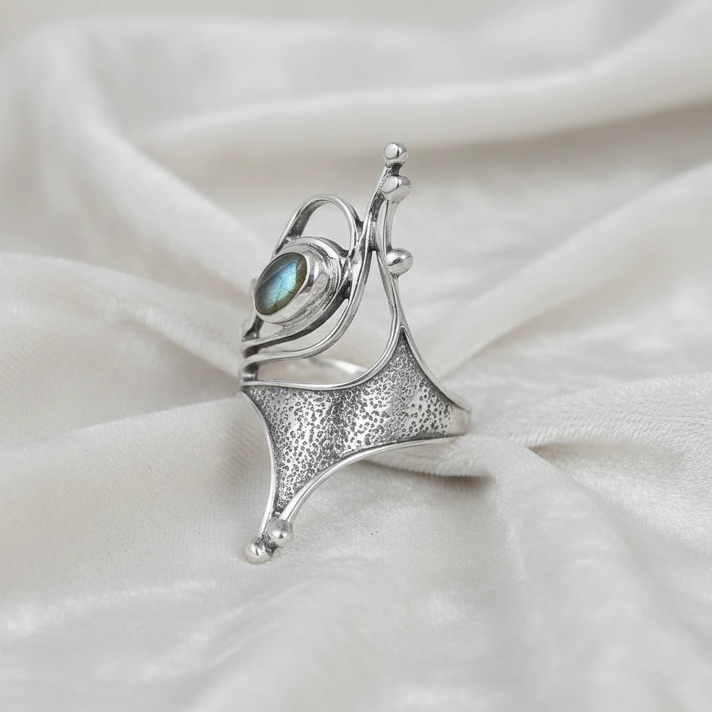 Sterling silver labradorite ring with an abstract sculptural design with textured metal viewed slightly angled on soft white fabric