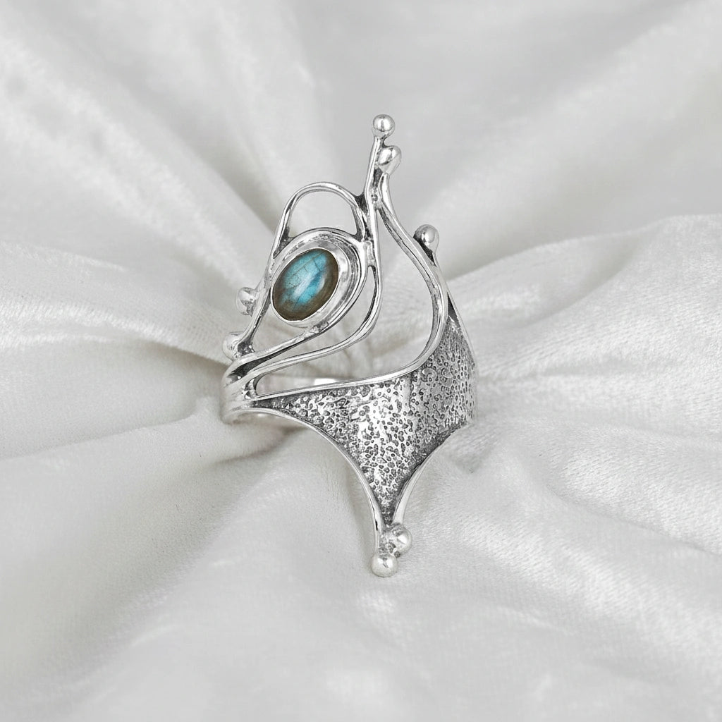 Sterling silver labradorite ring with an abstract sculptural design with textured metal viewed straight angled on soft white fabric