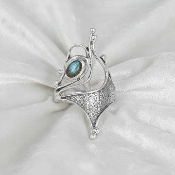 Sterling silver labradorite ring with an abstract sculptural design with textured metal viewed straight angled on soft white fabric