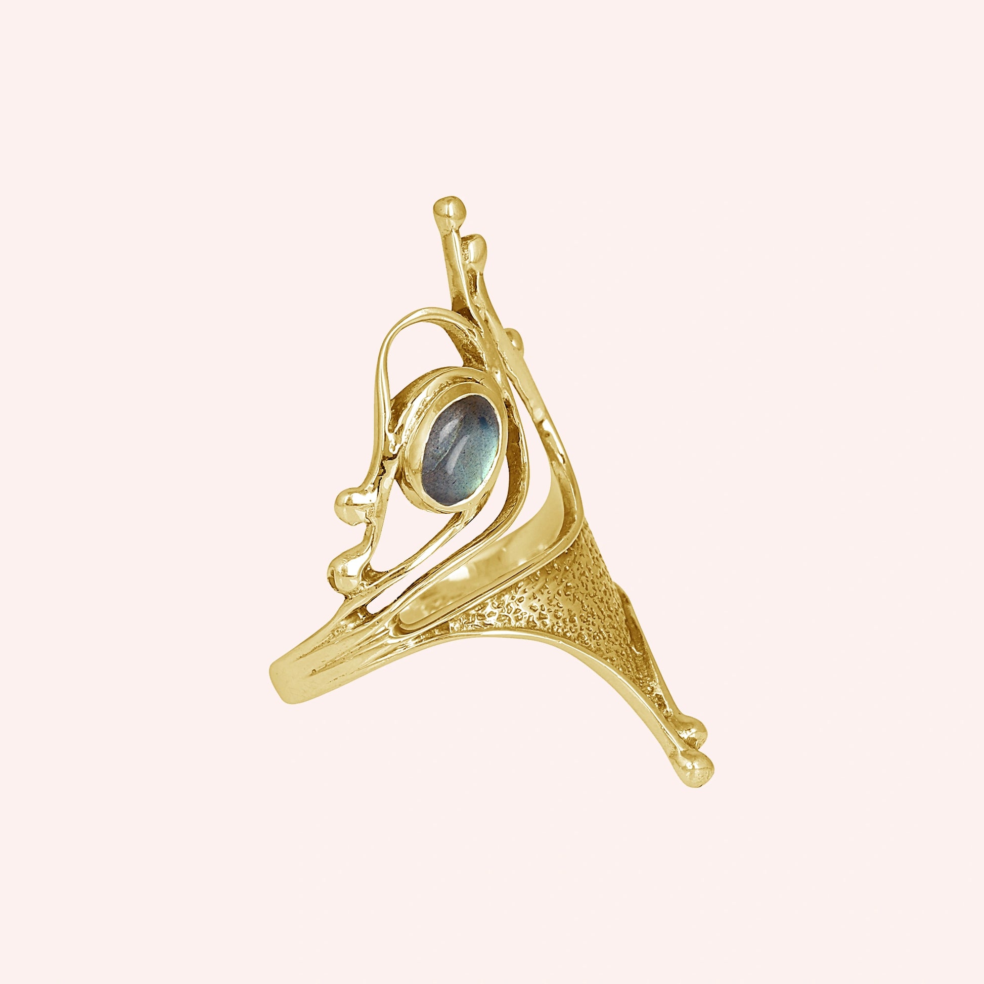 Gold-plated sterling silver labradorite ring with sculptural design and oval gemstone viewed slightly angled on pink background