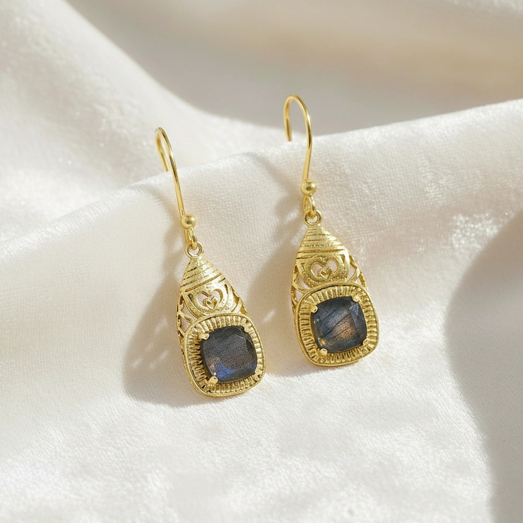 Gold-plated gemstone earrings filigree dangle design with square labradorite stone viewed slightly angled on white fabric