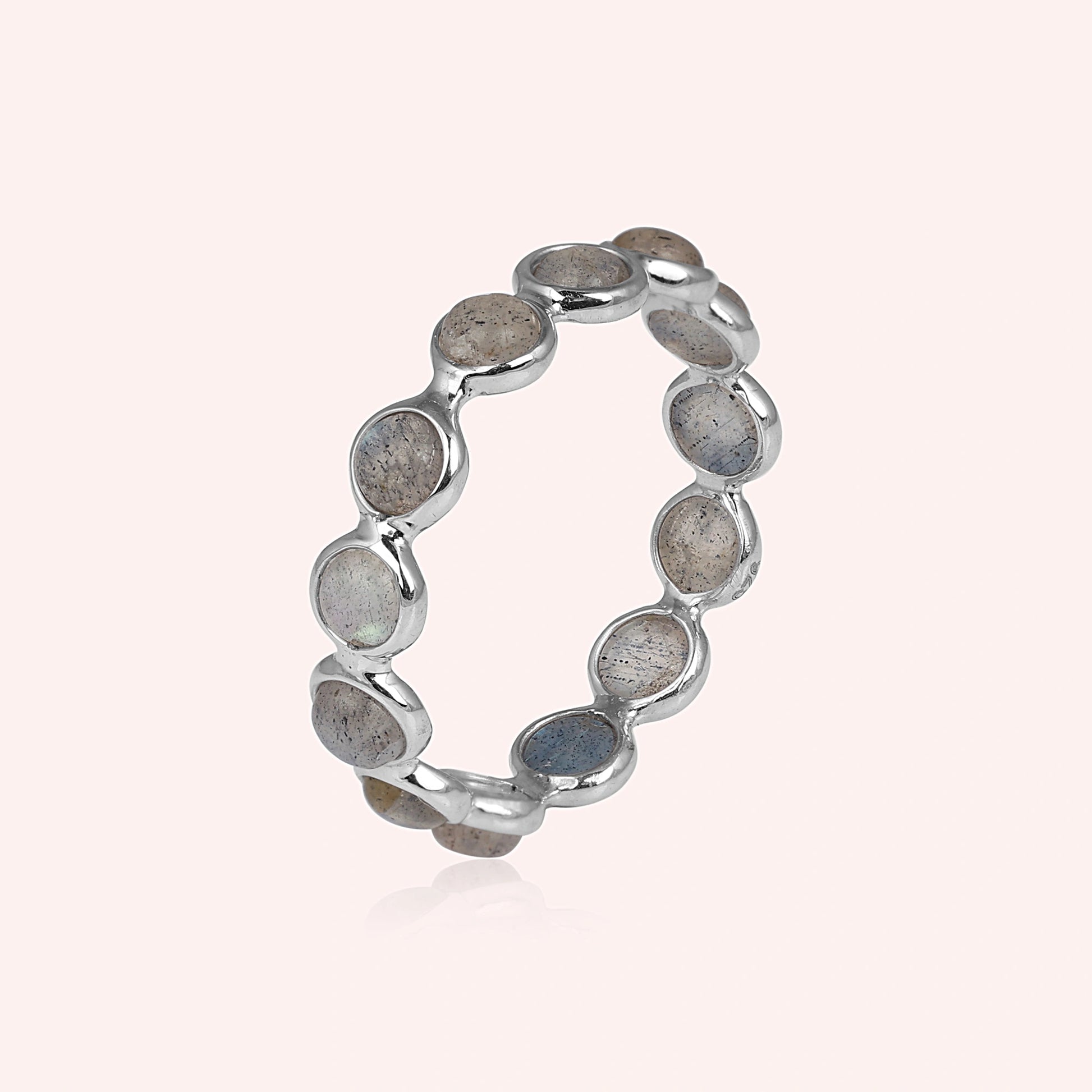 Angled shot of a sterling silver labradorite ring on a light pink background with round iridescent stones and slight reflection