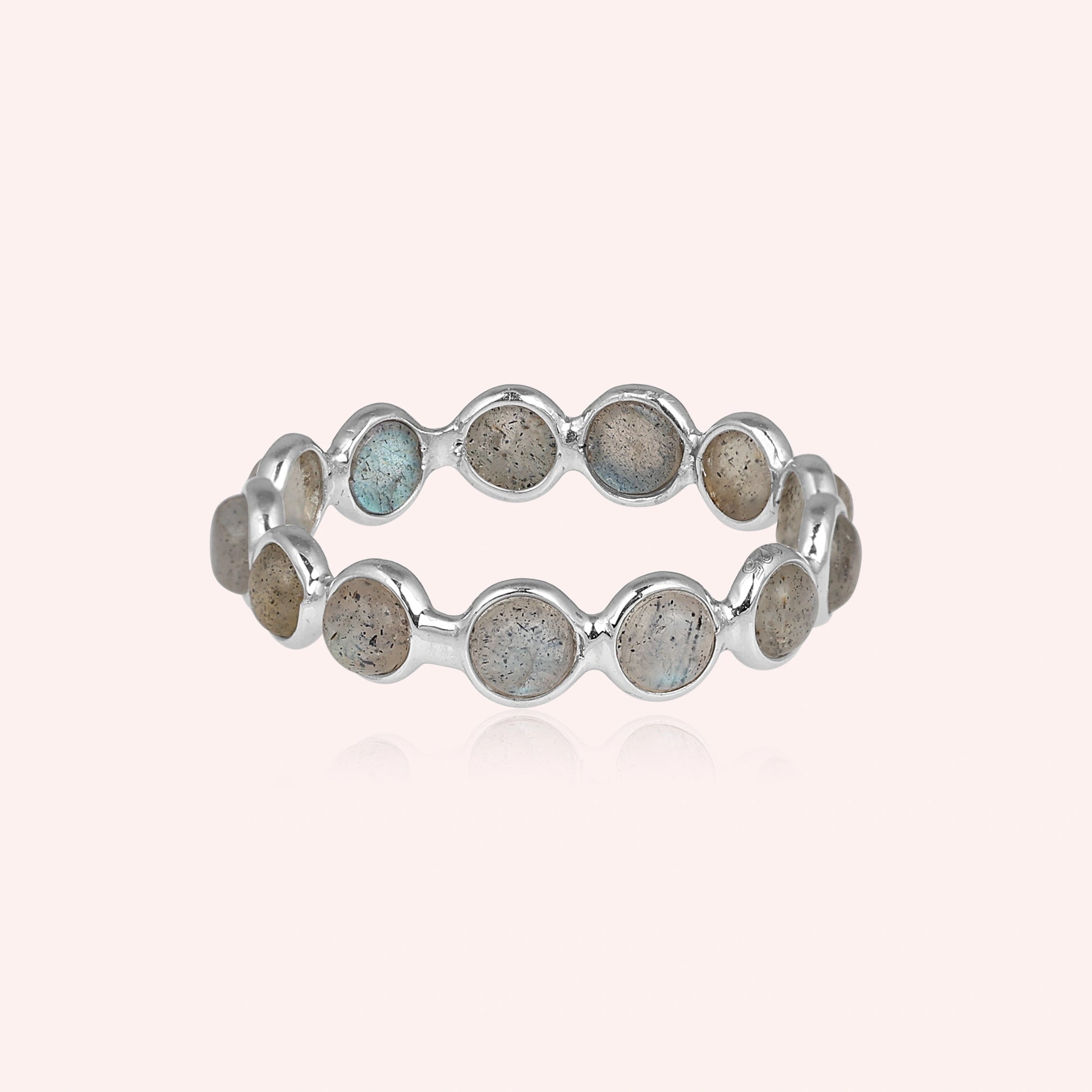 Horizontal shot of a sterling silver labradorite ring on a light pink background with round iridescent stones and reflection