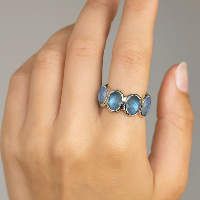 Silver labradorite ring with seven oval iridescent gray blue gemstones in the chunky setting shown at a slight angle on a white velvet.