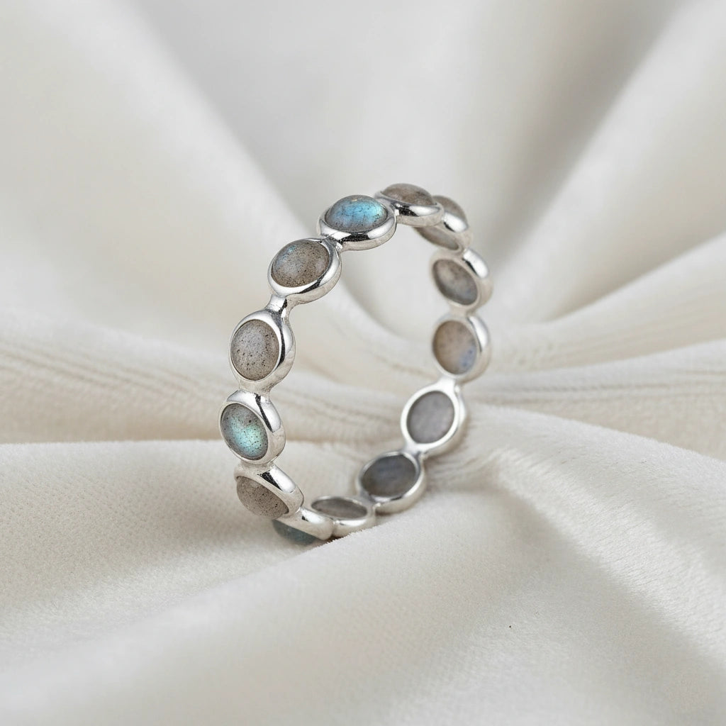 Angled close up shot of a sterling silver labradorite ring on an off-white velvet background with round iridescent stones