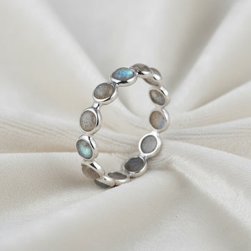 Angled close up shot of a sterling silver labradorite ring on an off-white velvet background with round iridescent stones